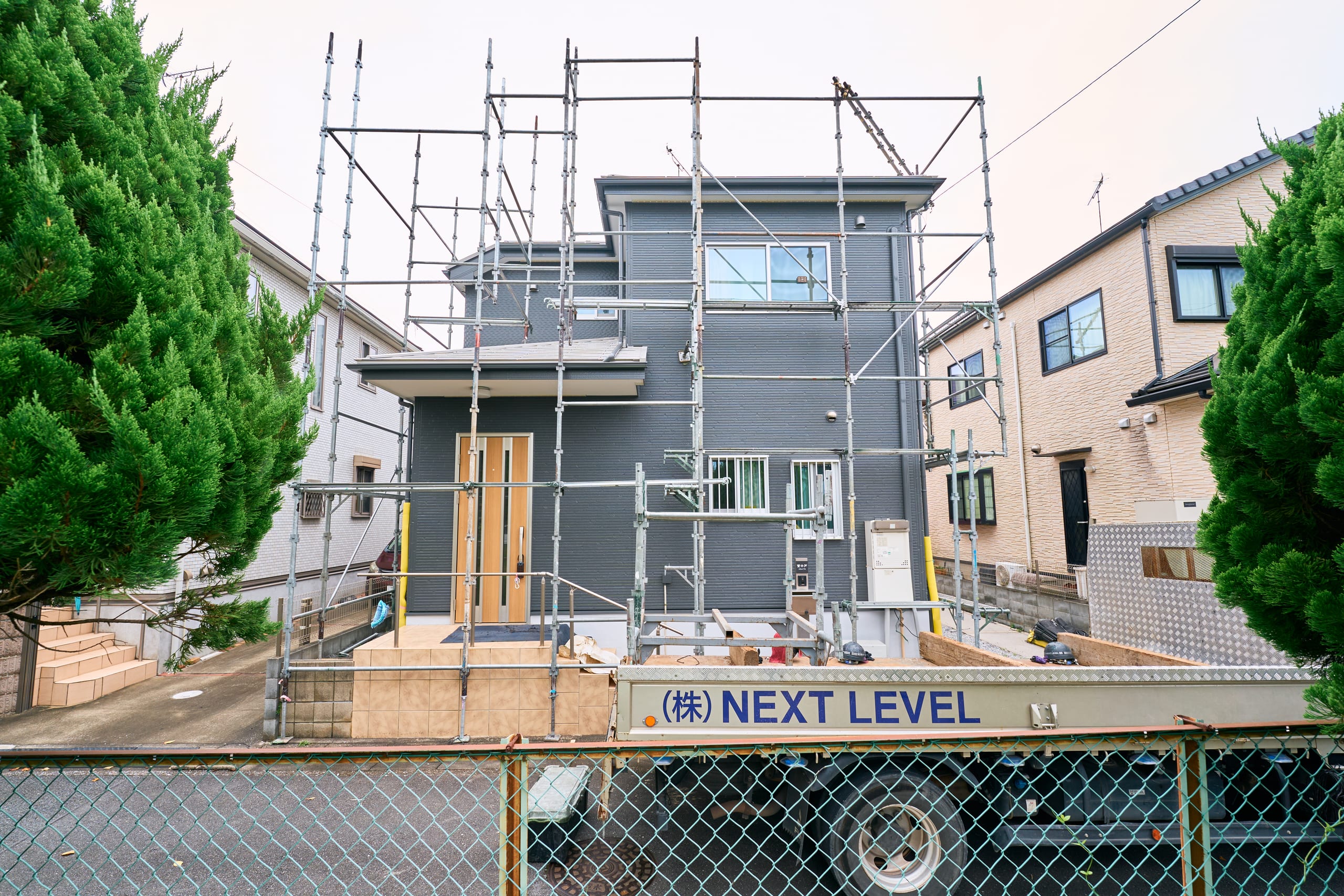 住宅を囲む足場とNEXT LEVELの作業車両