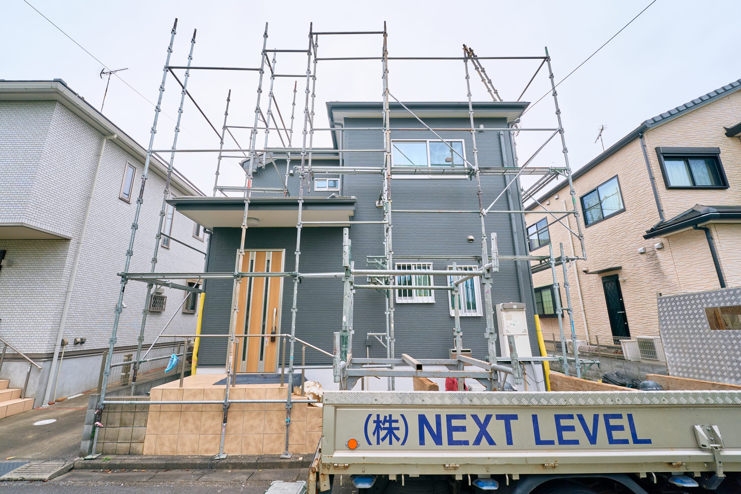 住宅を囲む足場とNEXT LEVELの作業車両